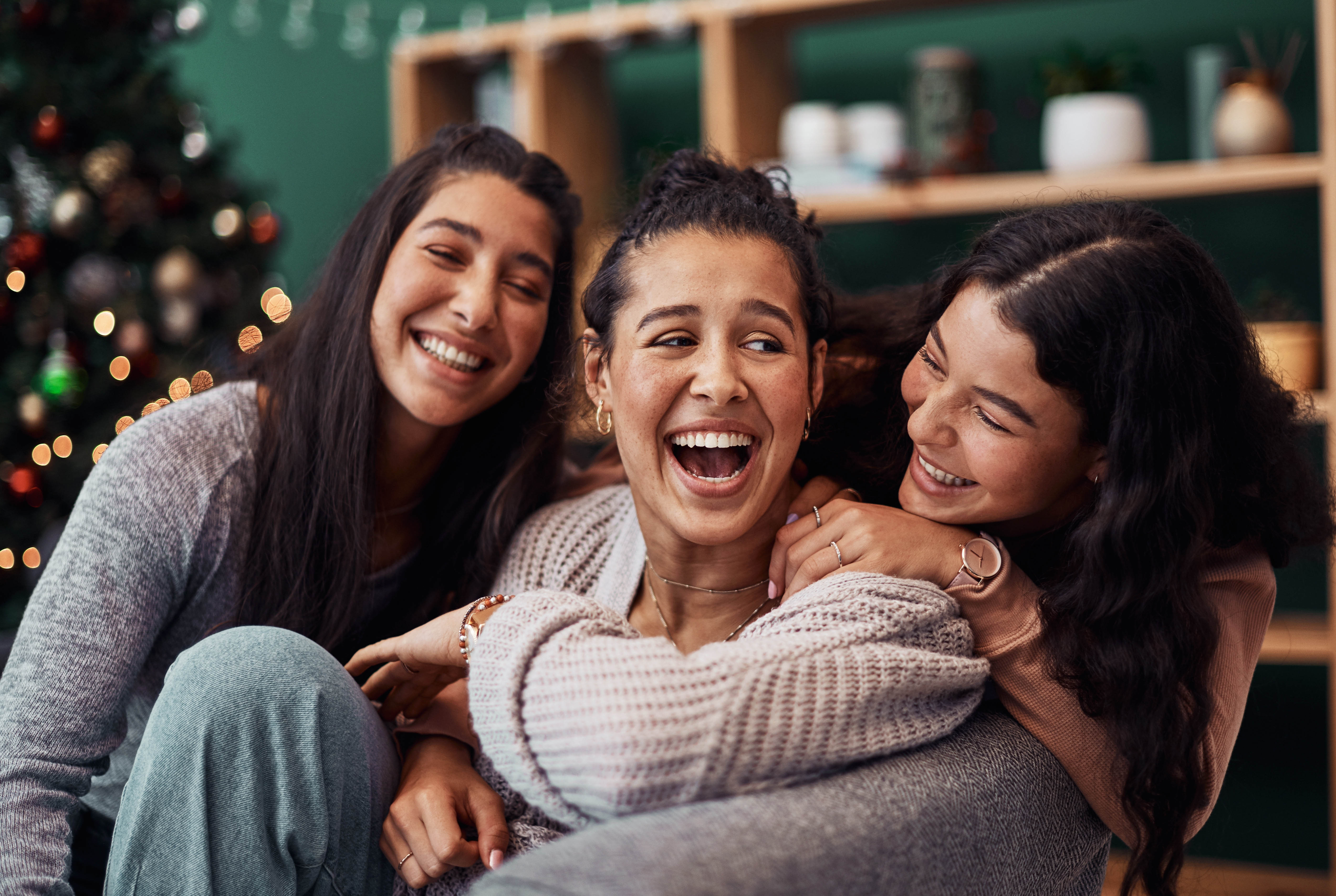 Three women sitting on the couch in front of the Christmas tree, laughing together Three women sitting on the couch in front of the Christmas tree, laughing together